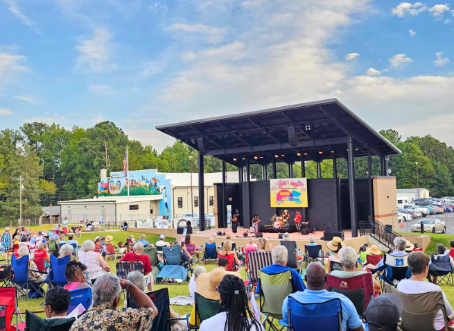Littleton residents of all backgrounds gather at the Ed Fitts Amphitheater for the first-ever Levitt AMP Littleton Music Series. The photo is rich in color and captures a sunny day in North Carolina. 